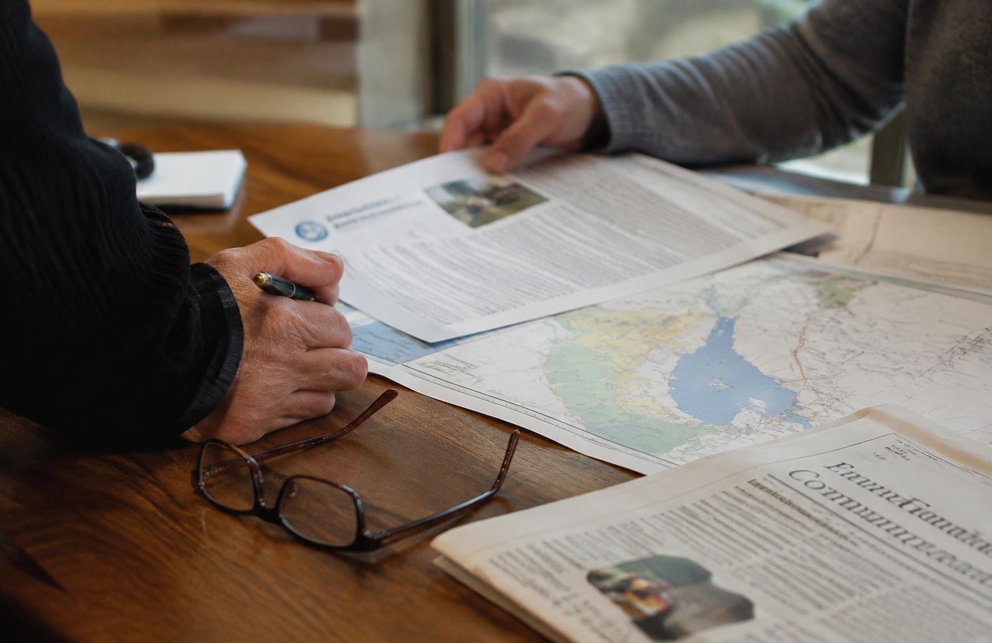 Hands reviewing printed municipal documents and a town map on a wooden table